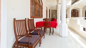 Un couloir avec des chaises et des tables en bois, des colonnes blanches et des fenêtres en arc de cercle.