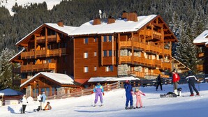 A wooden chalet with multiple balconies and a ski slope in front.