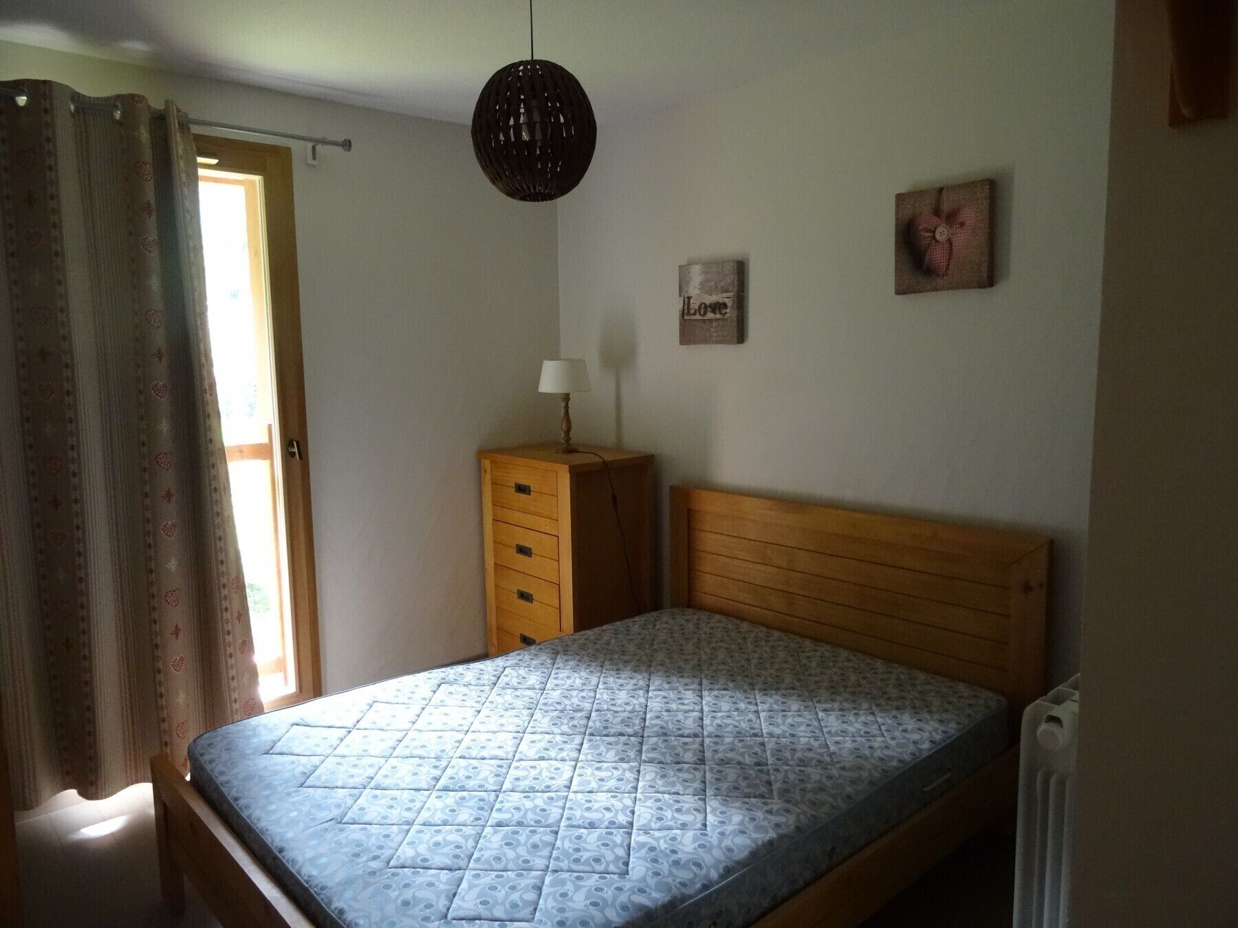 A bedroom with a wooden bed, a nightstand, a lamp, and a wall-mounted picture.
