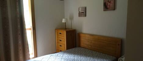 A bedroom with a wooden bed, a nightstand, a lamp, and a wall-mounted picture.