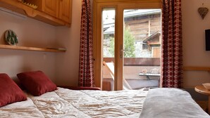 Un dormitorio con cama, almohadas rojas, cabecera de madera, ventana con cortinas y vista a un edificio de madera.