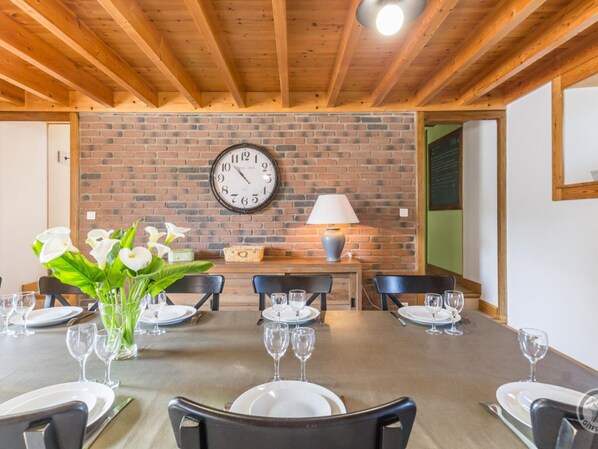 Un comedor con pared de ladrillo, un reloj y una mesa preparada para seis personas con sillas.