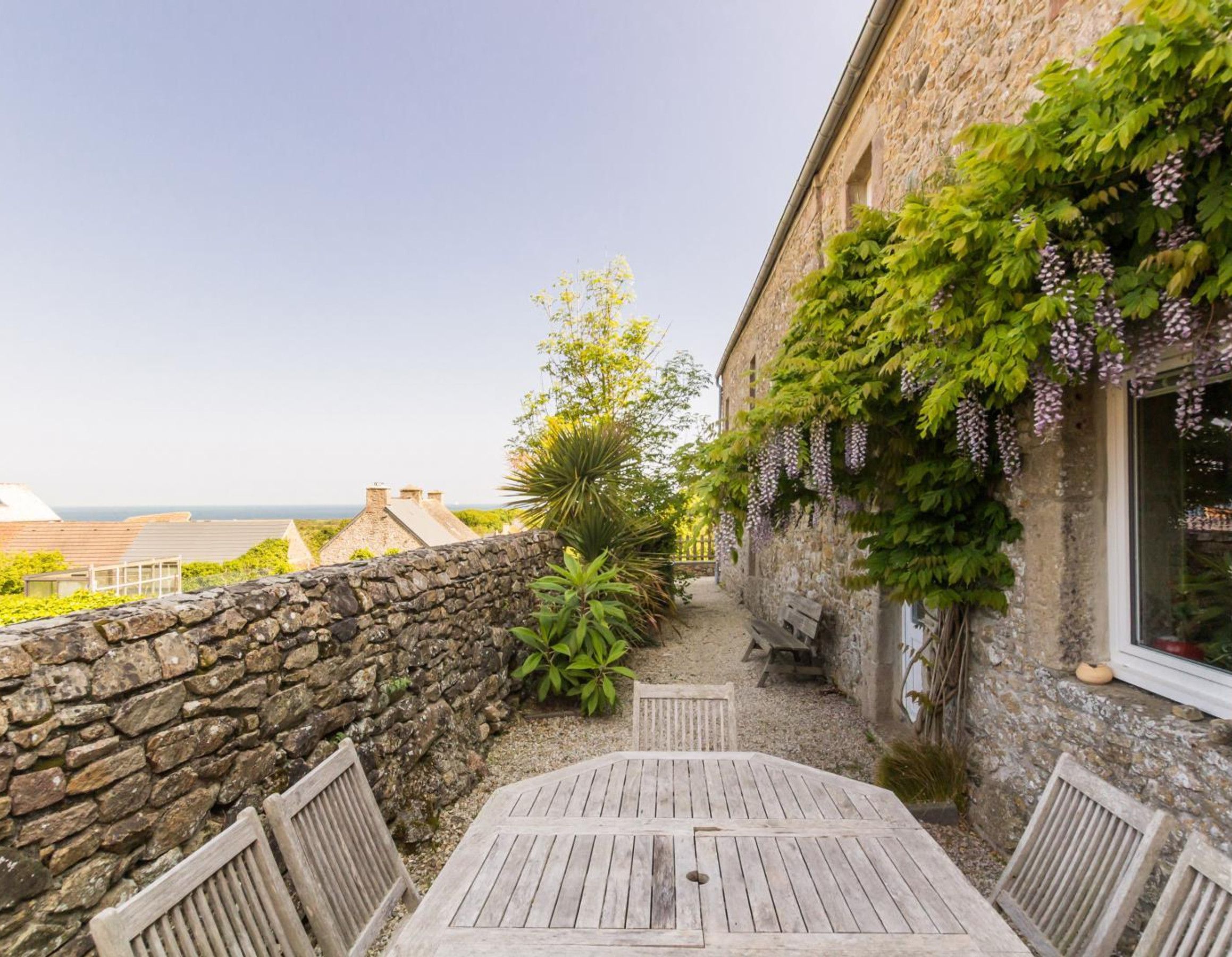 Un edificio de piedra con una mesa y bancos de madera, un muro de piedra y vistas al mar.