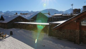 A snow-covered outdoor area with wooden buildings, a clear sky, and mountains in the background. - Sunny 3-Room Apartment for 6 with Large Terrace, Parking & Ski-In/Ski-Out Access (Huez)