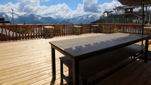 A wooden deck with a bench and a table, overlooking a mountainous landscape with a bridge in the background. - Sunny 3-Room Apartment for 6 with Large Terrace, Parking & Ski-In/Ski-Out Access (Huez)