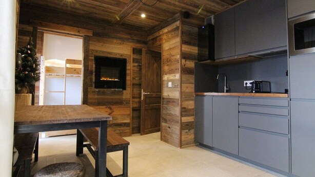 A modern kitchen with wooden accents, a dining area, and a fireplace. - Sunny 3-Room Apartment for 6 with Large Terrace, Parking & Ski-In/Ski-Out Access (Huez)