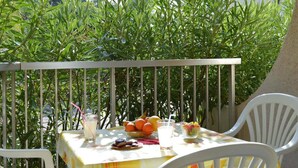 A table with fruits, a drink, and a bowl of cookies on a balcony with a railing and greenery in the background. - Ground Floor Apartment Near Port Santa Lucia with Terrace and Garage (Saint-Raphaël)