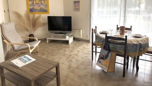 A living room with a flat-screen TV, a dining table with chairs, a sofa, and a large window with curtains. - Ground Floor Apartment Near Port Santa Lucia with Terrace and Garage (Saint-Raphaël)