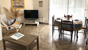 A living room with a TV, a dining table set for four, a sofa, and a chair. - Ground Floor Apartment Near Port Santa Lucia with Terrace and Garage (Saint-Raphaël)