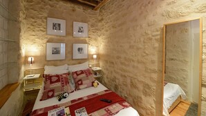 A cozy bedroom with a stone wall, a wooden ceiling, a bed with red and white bedding, a bedside table with a lamp, and framed pictures on the wall. - A1G Dreaming (París)