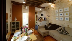 A cozy living room with a sofa, dining table set for a meal, and a kitchen in the background. - A1G Dreaming (París)