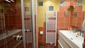 A bathroom with a glass shower enclosure, a white sink with toiletries, and a towel rack. - E5DD Yellow Cake (París)