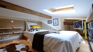 A bedroom with a skylight, a bed with pillows, a mounted TV, and a cowhide rug. - E5DD Yellow Cake (París)
