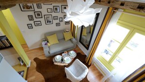 A cozy living room with a grey sofa, a white armchair, and a wooden coffee table. There are framed pictures on the wall and a large white light fixture above the sofa. - E5DD Yellow Cake (París)