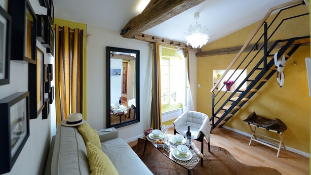 A cozy living room with a sofa, a dining table set for a meal, a chair, and a staircase. - E5DD Yellow Cake (París)