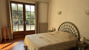 Ein Schlafzimmer mit einem Bett, einem Nachttisch, einer Lampe, einem Sessel und einem Fenster mit Vorhängen.
