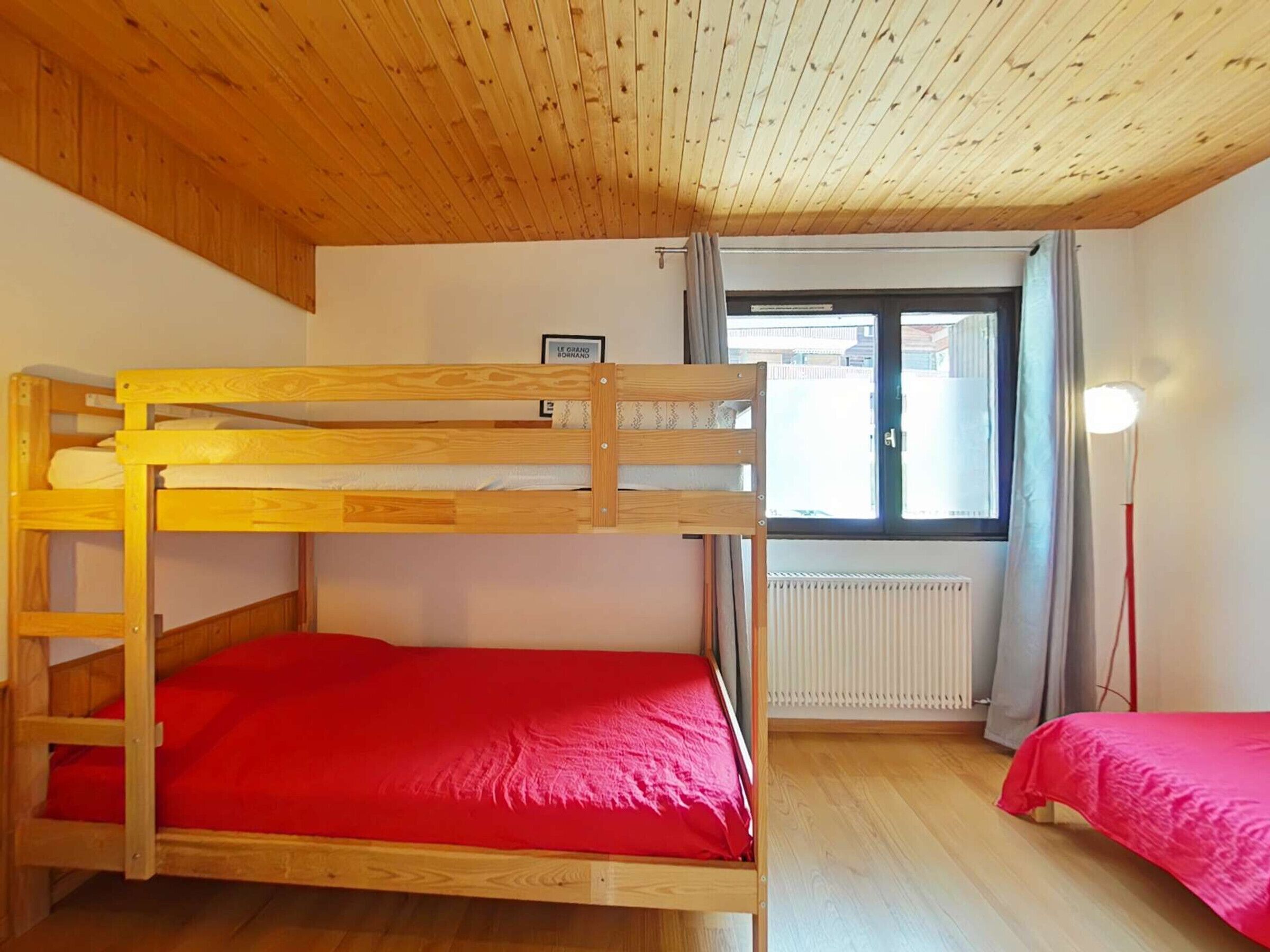 Una habitación con dos literas, una ventana con cortinas, un radiador y un techo de madera.