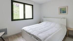 A bedroom with a bed, a window, a radiator, a desk, and a painting on the wall.
