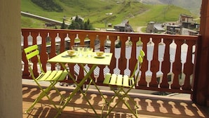A balcony with a table and chairs, overlooking a mountainous landscape.