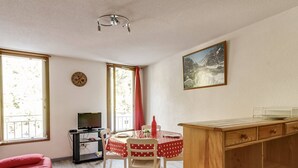 A compact room with a bed, a dining table with chairs, a TV, and a painting on the wall.