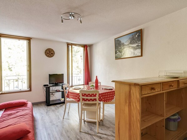 Quarto compacto com cama, mesa de jantar com cadeiras, televisão e um quadro na parede.