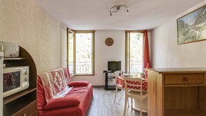 A compact living space with a sofa, a TV, a dining table with chairs, and a wooden cabinet.
