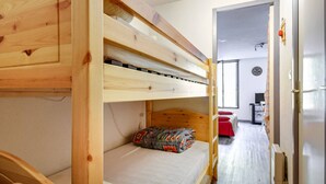 A bunk bed room with a wooden headboard, a single bed with a patterned pillow, and a desk with a chair in the background.