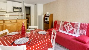 A compact living space with a kitchenette, a dining area with a red polka dot tablecloth, and a red sofa with a quilted cover.