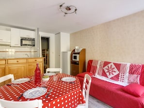 Um espaço compacto com cozinha americana, área de refeições com toalha de mesa vermelha com bolinhas e sofá vermelho com capa acolchoada.