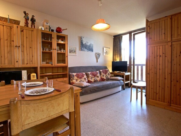 A cozy living room with a sofa, wooden cabinets, a dining table, and a television.