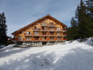 A multi-story wooden building with balconies, surrounded by snow and trees.