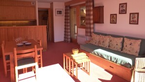 A cozy living room with a wooden dining table, a sofa with patterned cushions, and a small wooden stool. - Cozy apartment in Méribel Altiport, 2 rooms, sleeps 6, pets allowed (Méribel)