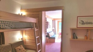 A cozy room with a bunk bed, a sofa, a ladder, a framed picture on the wall, and a doorway leading to another room. - Cozy apartment in Méribel Altiport, 2 rooms, sleeps 6, pets allowed (Méribel)