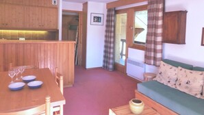 A compact living space with a wooden dining table, a green sofa, and a kitchen area with wooden cabinets. - Cozy apartment in Méribel Altiport, 2 rooms, sleeps 6, pets allowed (Méribel)