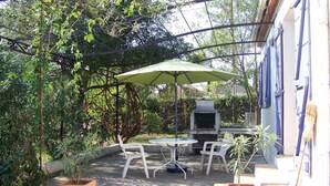 Un patio al aire libre con mesa y sillas, una sombrilla verde y una parrilla de barbacoa.