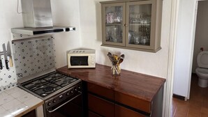 Una cocina compacta con estufa a gas, microondas y un armario con puertas de vidrio.