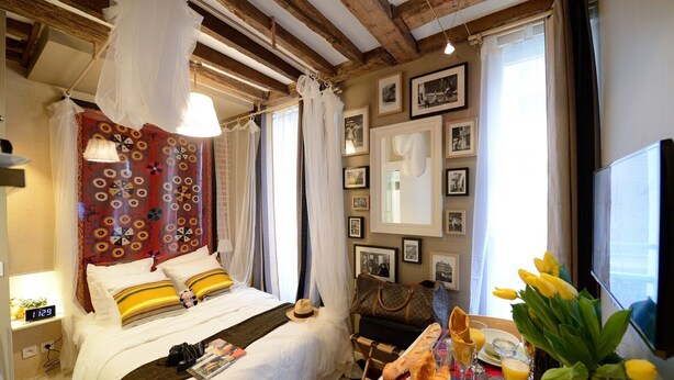 Um quarto acolhedor com cama, mesa de cabeceira com itens de café da manhã, televisão e parede com quadros.