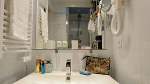 Uma casa de banho moderna com uma sanita branca, um espelho e um chuveiro visível ao fundo.