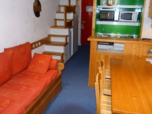 Cozy retreat with a sofa, table, and kitchenette, featuring a staircase to an upper level.