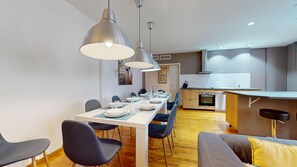 A modern kitchen with a dining area, featuring a long table set for four, overhead pendant lighting, and a built-in oven and dishwasher. - lacour ac 160m2 city center  4br3bth (Colmar)