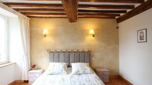 A bedroom with a wooden ceiling, two bedside lamps, a bed with floral bedding, and a small nightstand. - Stone house in peace with pets allowed (Ouville)