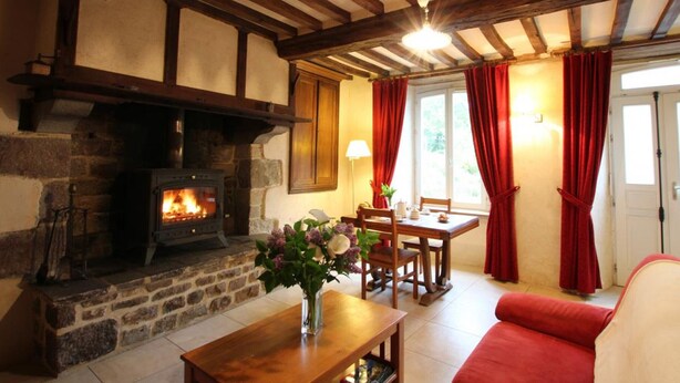 A cozy living room with a stone fireplace, wooden beams, a dining area, and red curtains. - Stone house in peace with pets allowed (Ouville)
