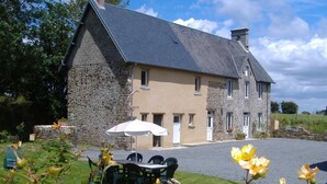 A stone building with a sloped roof, a paved driveway, and a table with chairs in the foreground. - Stone house in peace with pets allowed (Ouville)