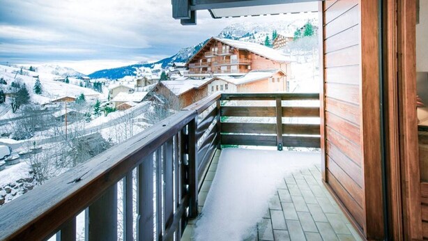 Een balkon met houten spijlen met uitzicht op een besneeuwd bergdorp.