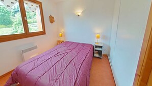 Een slaapkamer met een bed, twee bedlampen, een radiator en een raam met gordijnen.