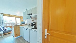 Een kleine keuken met witte apparaten, een houten deur en uitzicht naar buiten.