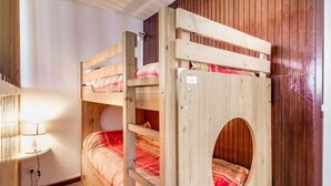 A bunk bed with a circular window in a room with wooden walls and a lamp on a side table.