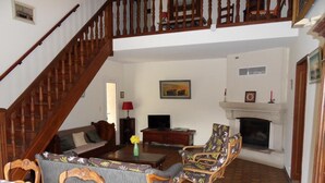 Una sala de estar con escalera de madera, chimenea, sofá, mesa de centro y televisor.