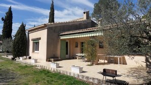Una casa de estilo mediterráneo con techo de tejas, puerta verde y un patio con mobiliario exterior.