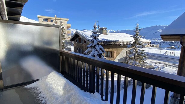 A balcony with a metal railing, snow-covered ground, and a view of buildings and snow-covered trees in a mountainous area. - Cozy 2-Room Apartment for 6 in Alpe d'Huez, Ski-in/Ski-out, Near Shops, South-Facing Balcony (Huez)